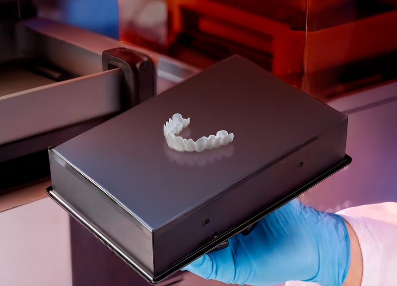 A finished white veneer arch on a 3D printer build platform held by a gloved hand